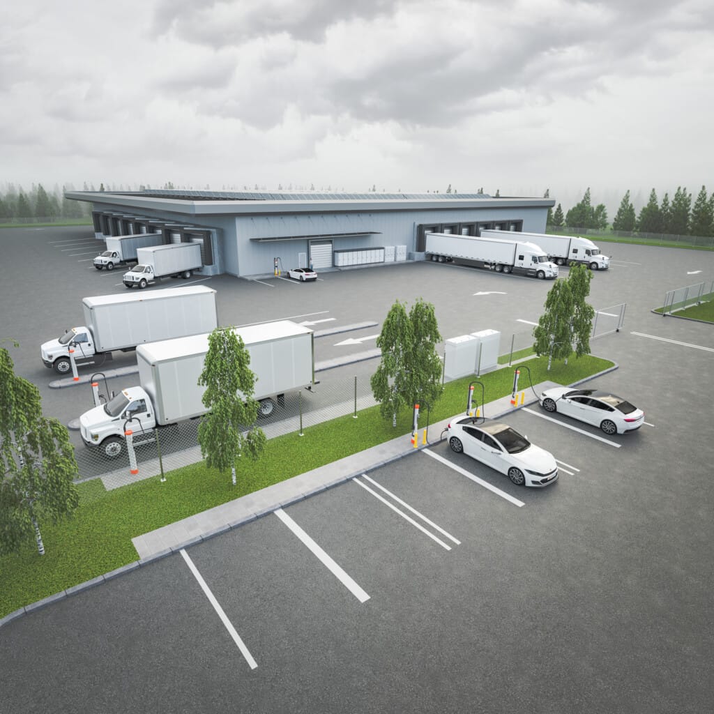 Aerial view of a transportation logistics center with several trucks and cars parked in a large parking lot next to a modern, low-rise warehouse on an overcast day.