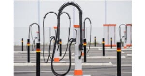 Empty electric vehicle charging stations with tall, flexible cables stand in a lined-up pattern in a parking lot.