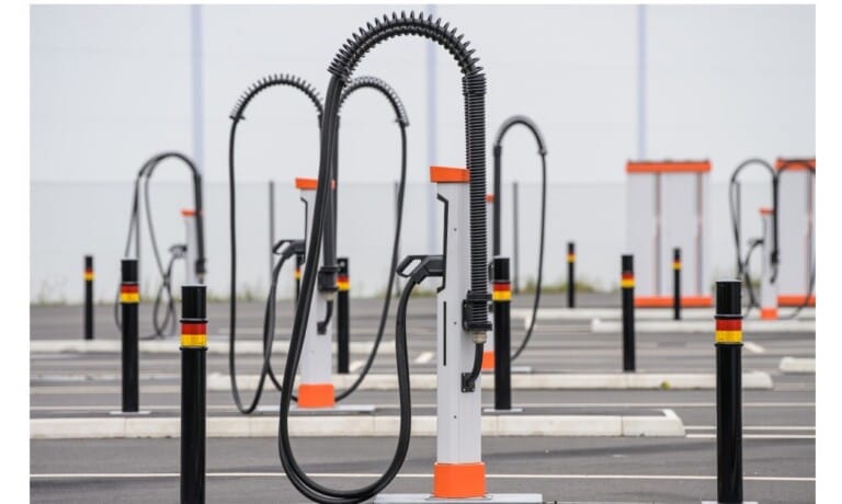 Empty electric vehicle charging stations with tall, flexible cables stand in a lined-up pattern in a parking lot.